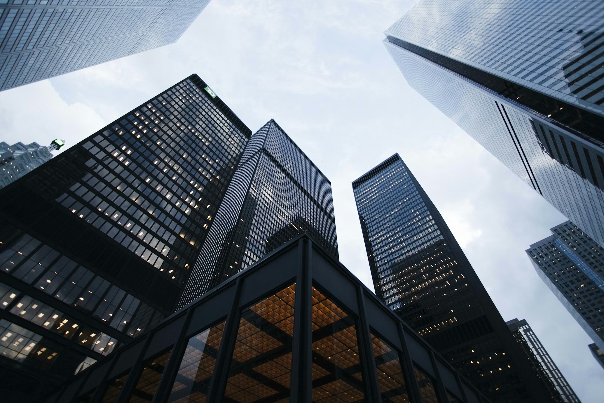Low-angle view looking up at a cluster of tall dark glass office towers converging against an overcast sky